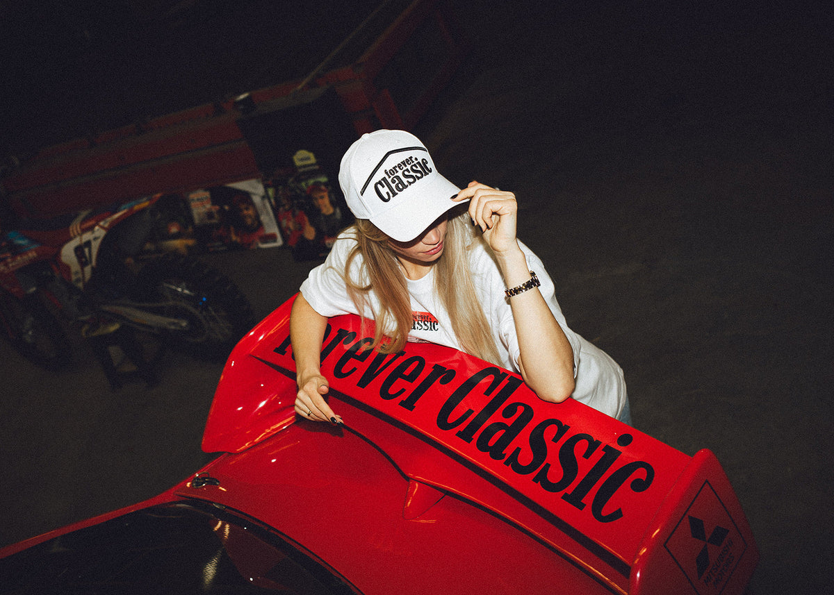 Forever Classic caps collection with a woman wearing a white logo cap beside a red Mitsubishi rally car