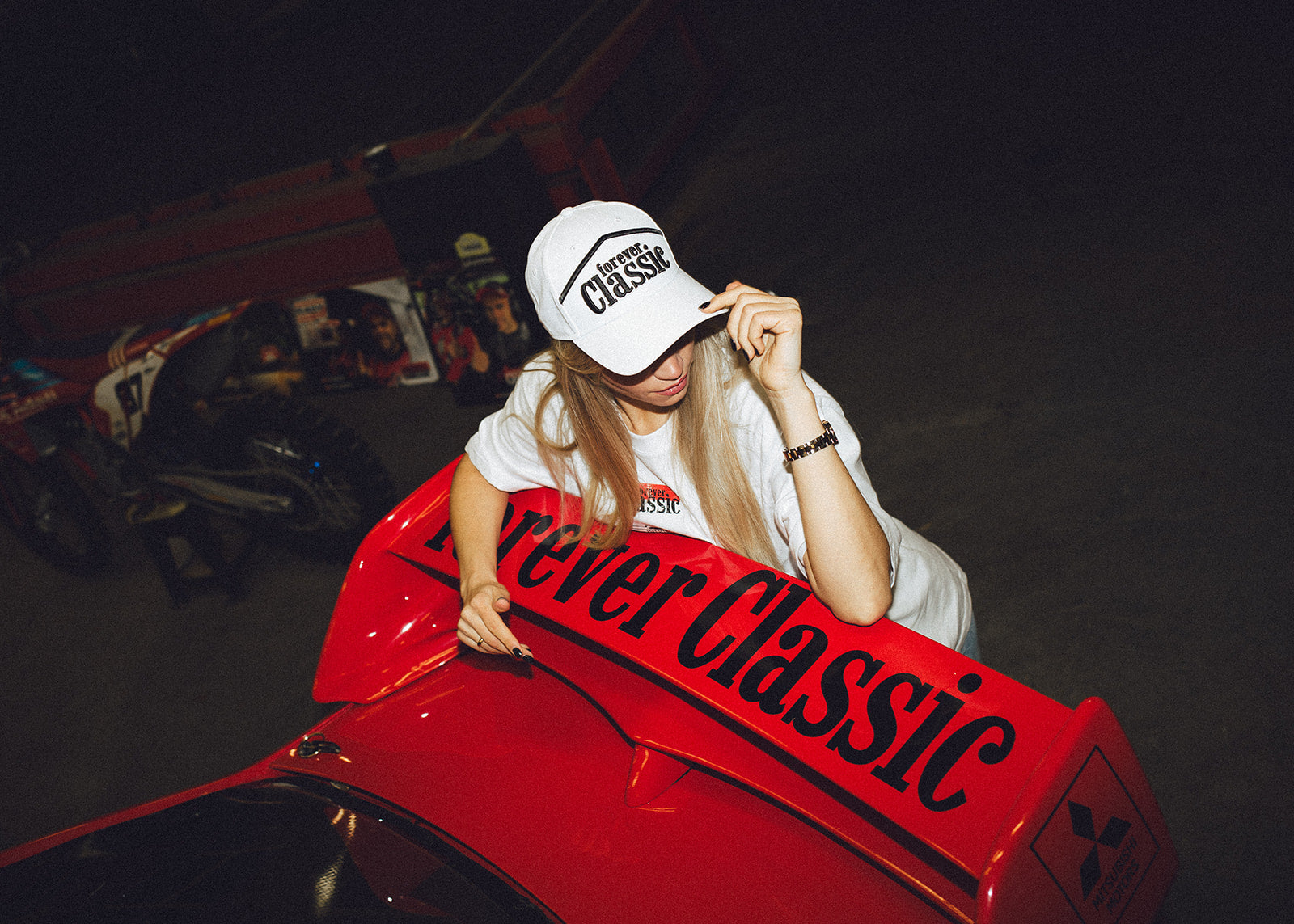 Forever Classic caps collection with a woman wearing a white logo cap beside a red Mitsubishi rally car