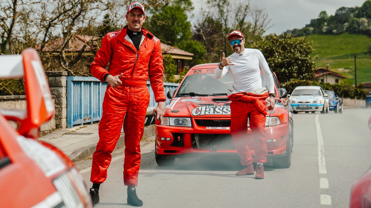 Rally crew in red race suits posing with the red Mitsubishi Lancer Evo on a closed road
