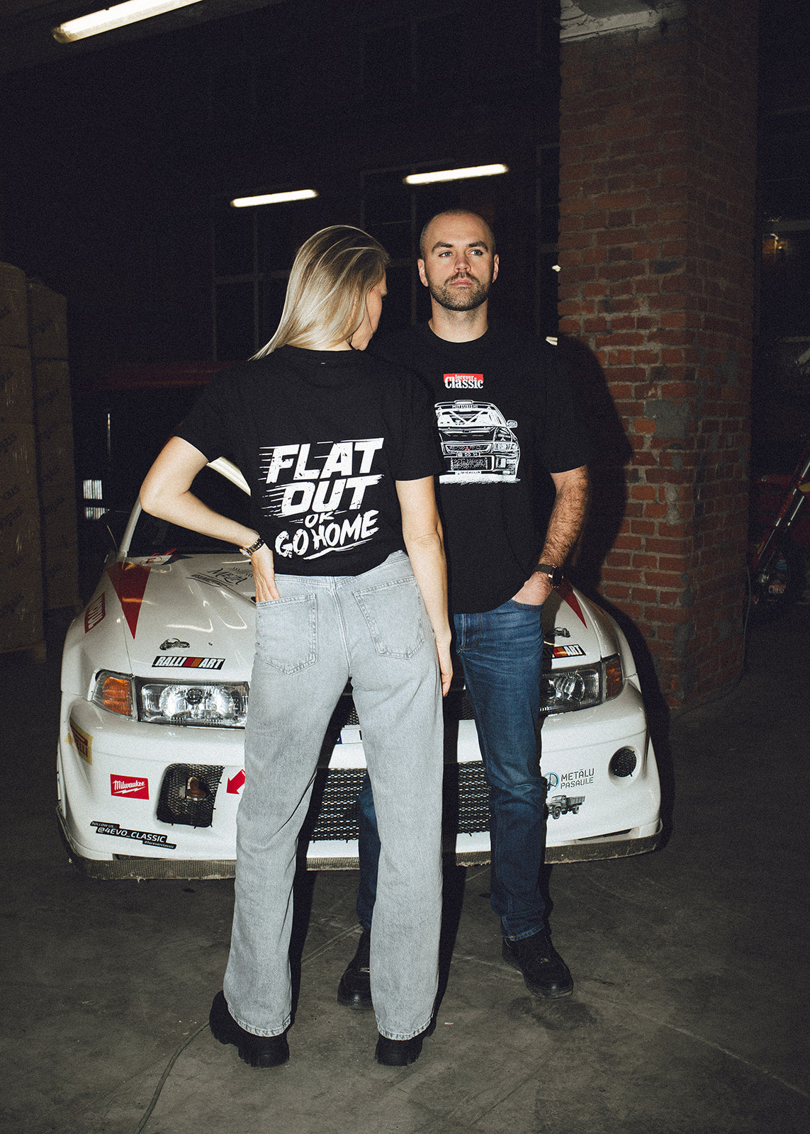 Back print of Flat Out or Go Home t-shirts worn by a couple in the race garage